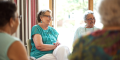 Seniorinnen sitzen als Gruppe und lächeln.