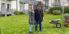 Dudenhofen: Stellvertretende Pflegedienstleiterin neben Bewohner und Kirschbaumpate vor Baum.