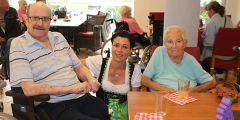 Schifferstadt: Mitarbeiterin in Dirndl zwischen Bewohnerin und Bewohner am Tisch.