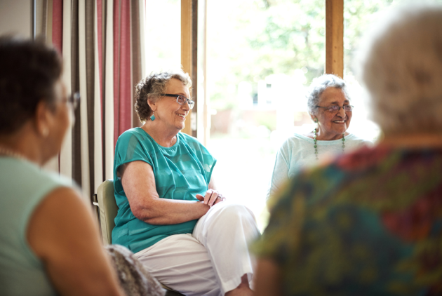 Seniorinnen sitzen als Gruppe und lächeln.